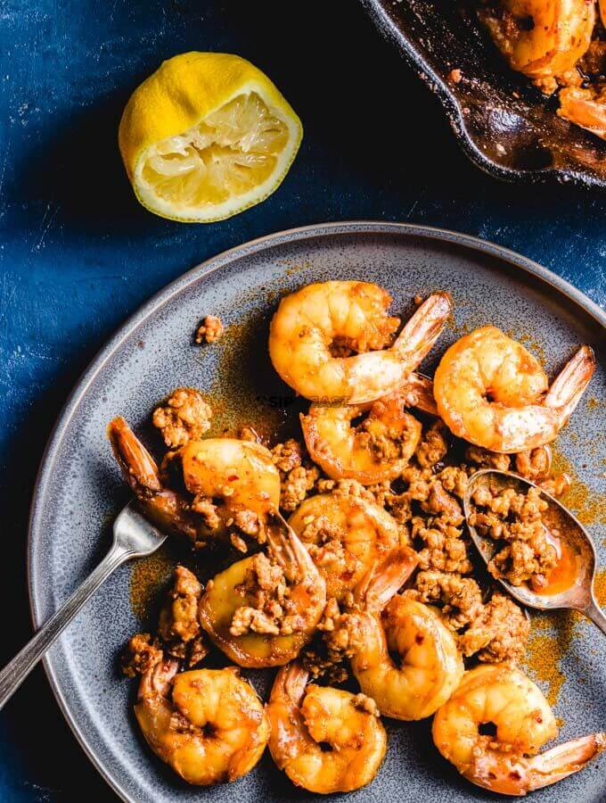 Chorizo and shrimp in grey plate with half a squeezed lemon on the side.