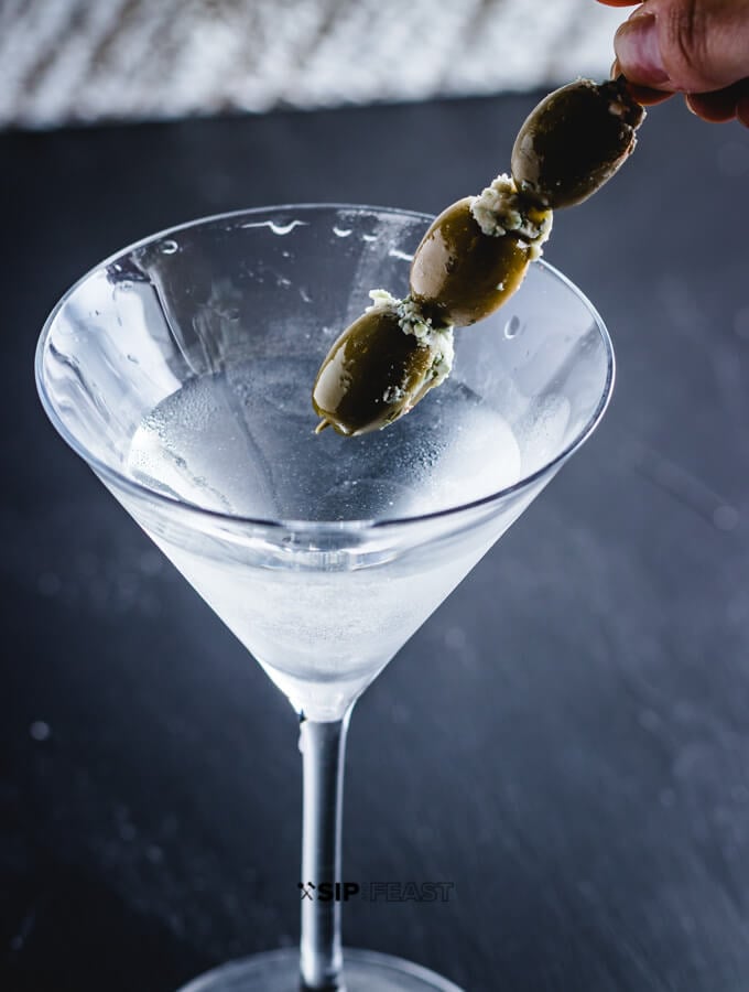 Placing 3 blue cheese olives into the martini.