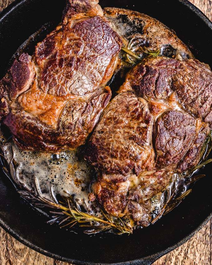 Picture of ribeyes in cast iron pan with rosemary. 