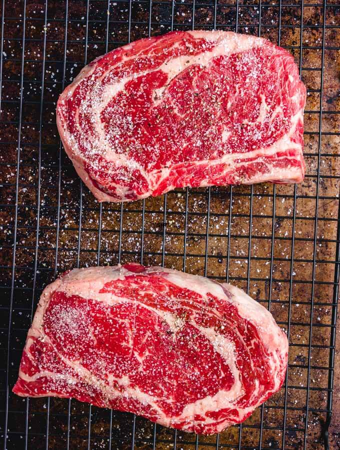 Salt and pepper on ribeyes on wire rack.