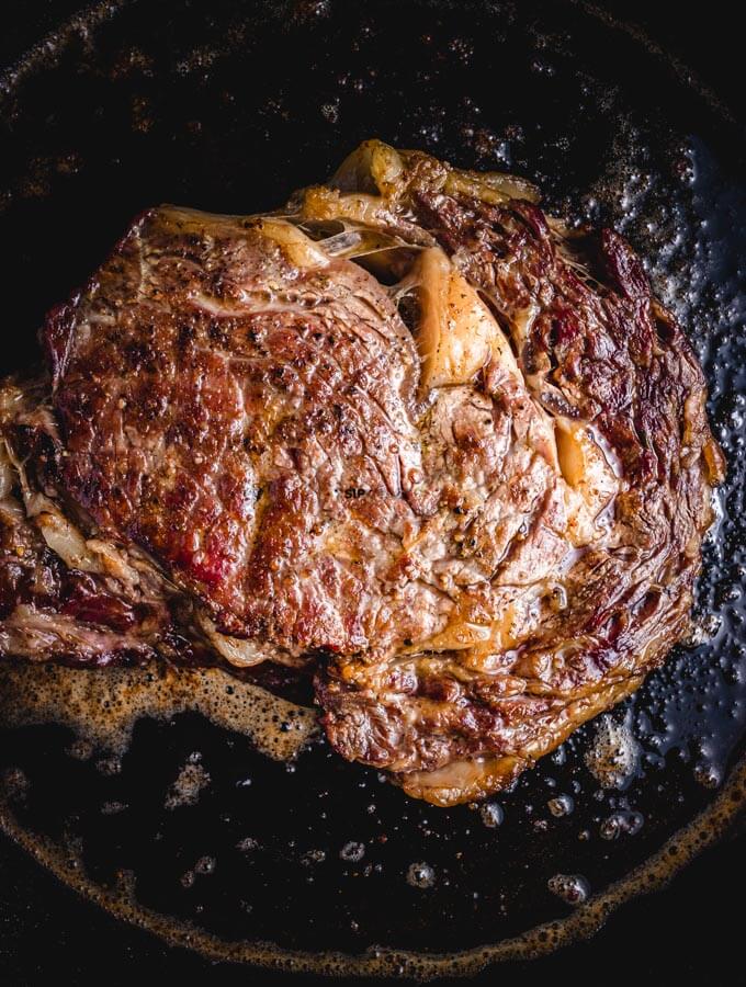 Cooking ribeye steak in cast iron pan.