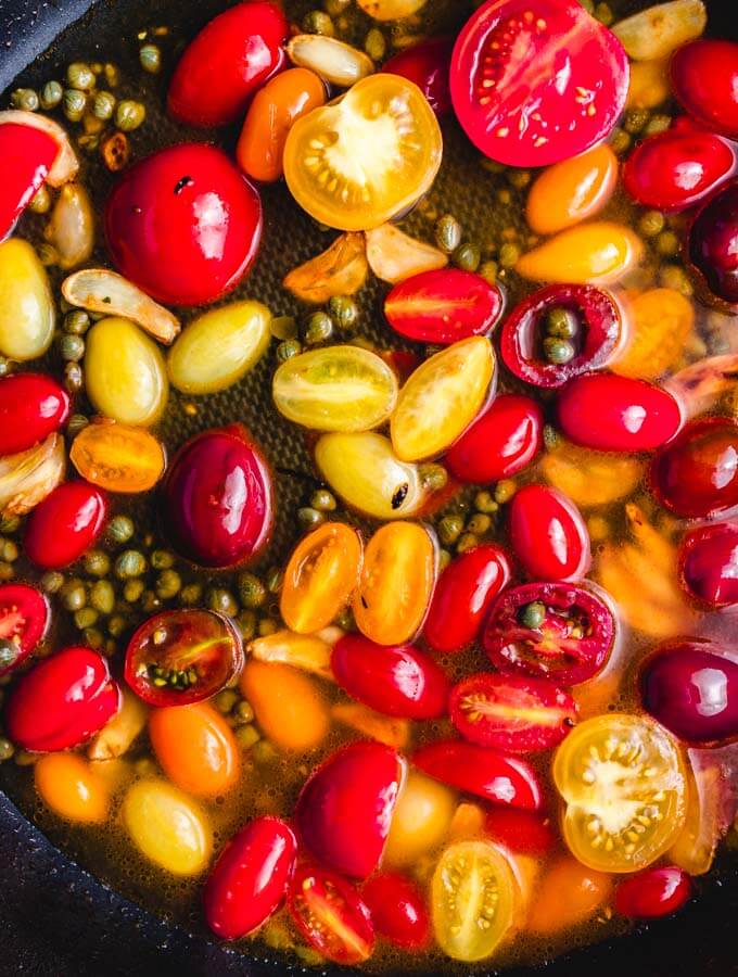 Added the cherry tomatoes, vinegar, water, garlic, and capers to the pan.