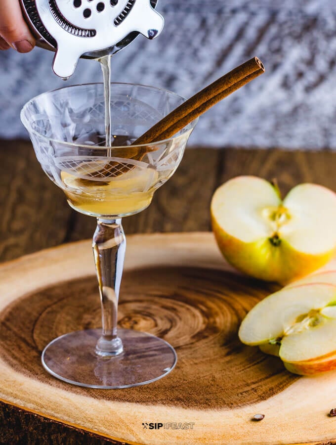 A cocktail shaker pouring the Apple cider cocktail with maple syrup and bourbon.