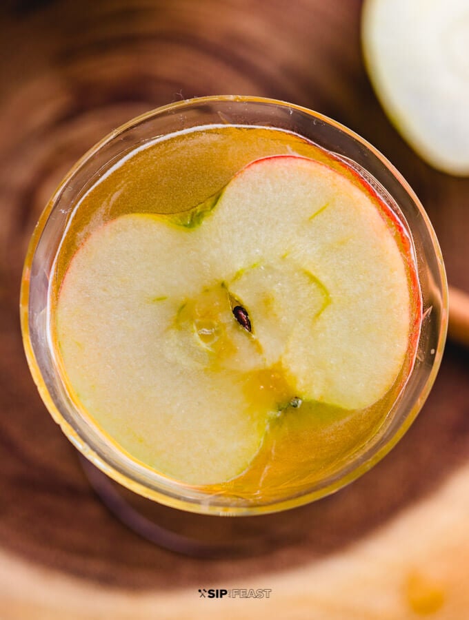 Overhead view of the glass with the apple cider cocktail and a slice of apple.