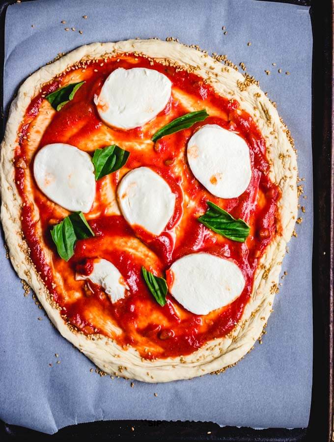 The garlicky tomato sauce, fresh mozzarella, and basil on the rolled out store bought pizza dough.