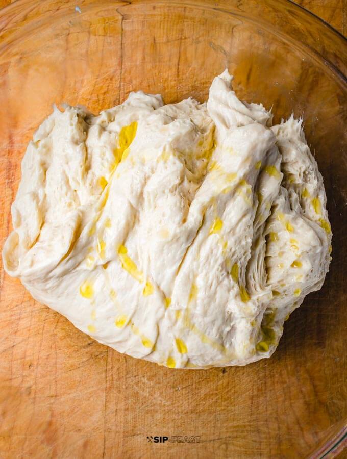 Store bought pizza dough in glass bowl with olive oil on top.