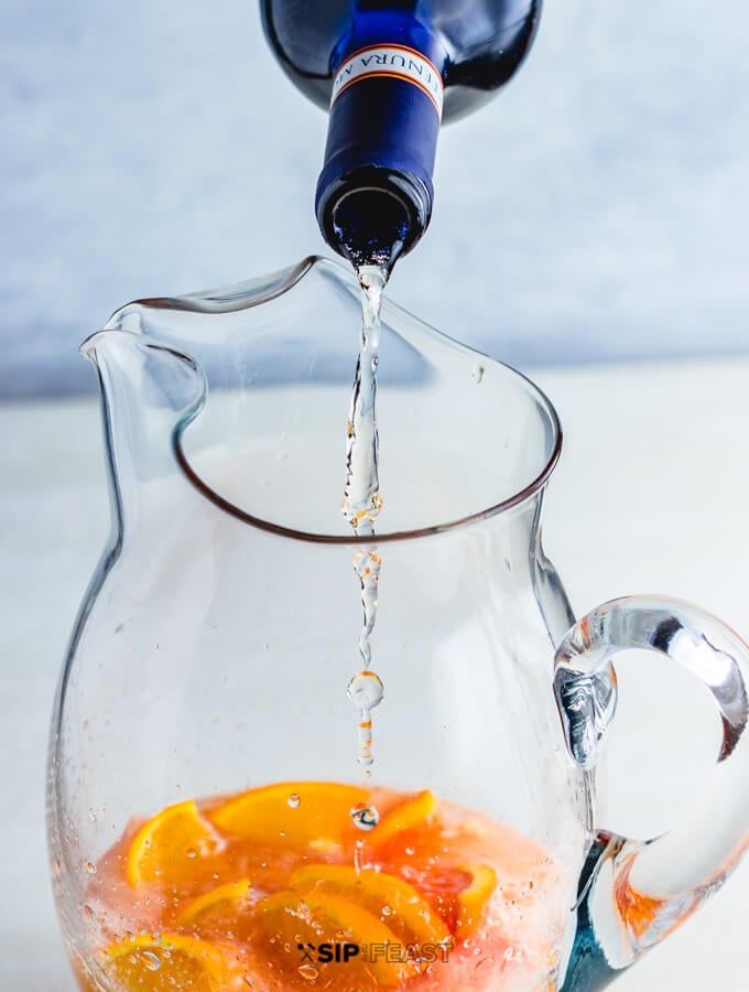 Moscato Sangria Pitcher with Oranges and Moscato being poured.