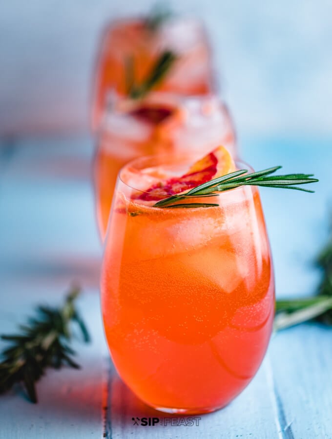 Aperol Spritz cocktail in three wine glasses with orange and rosemary garnish.