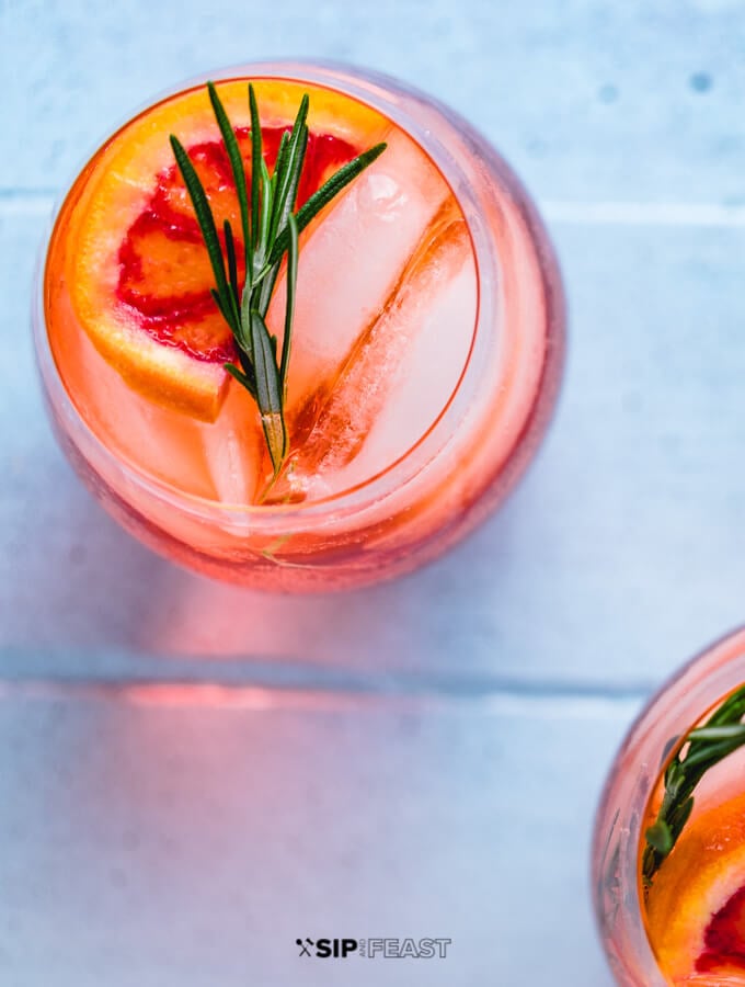 Aperol Spritz in wine glass with ice, rosemary and orange slice.