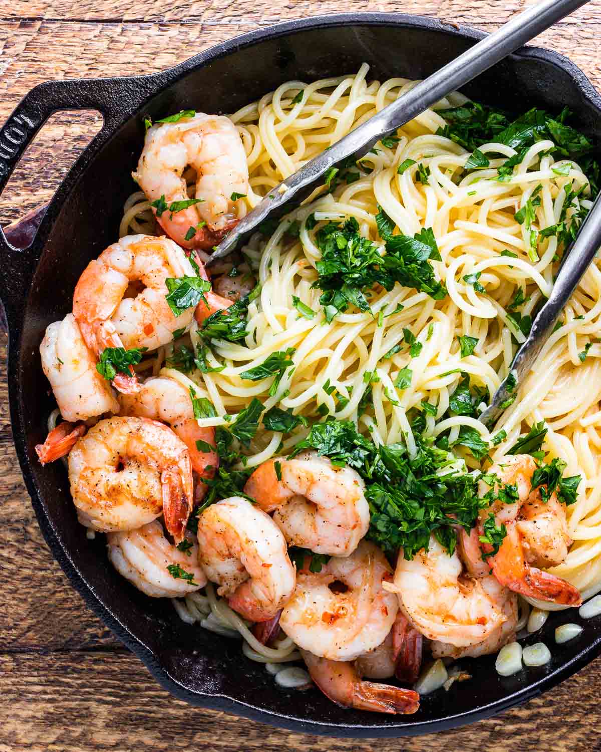 Lemon garlic shrimp pasta in black pan with tongs.