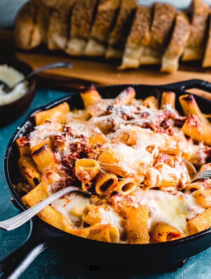 Baked pasta in cast iron pan with bread in background.