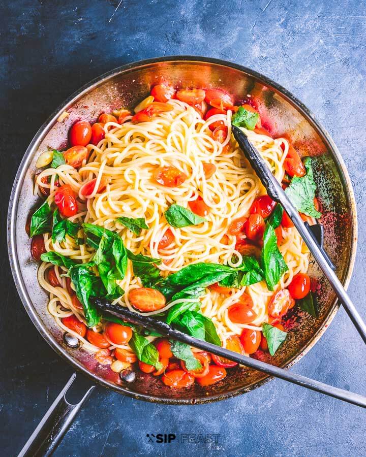 Finished pasta with cherry tomatoes , basil and garlic in the pan on top of blue setting.