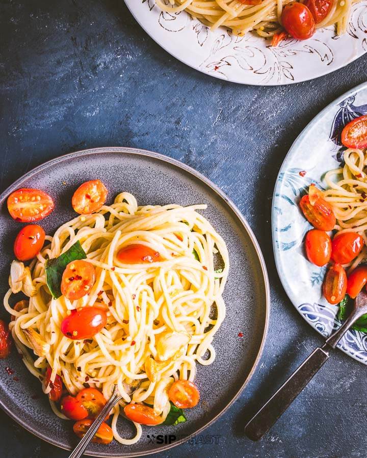 Three plates of spaghetti and tomatoes on blue background.