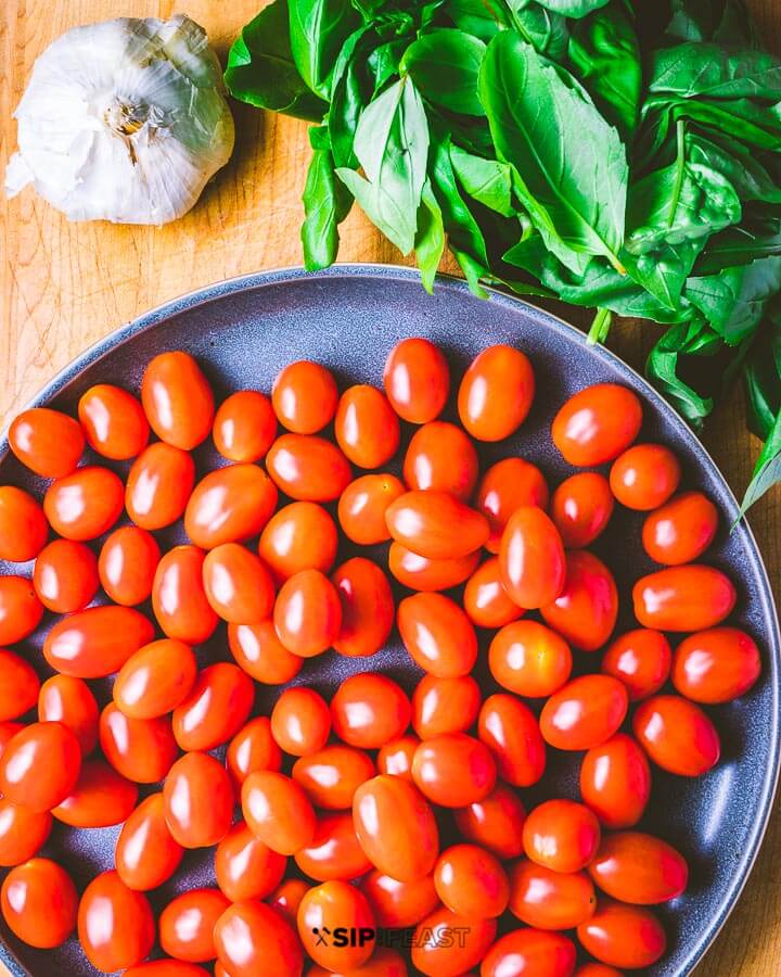 Large plate of cherry tomatoes, garlic and basil on cutting board.