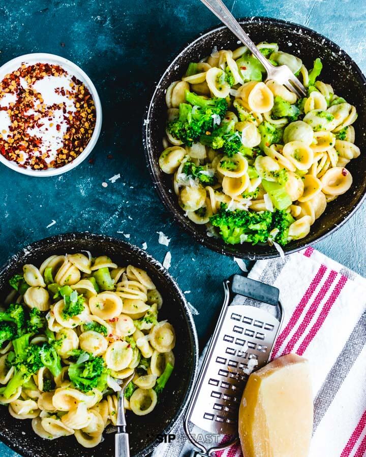 Two bowls of pasta and broccoli with pecorino cheese and grater.