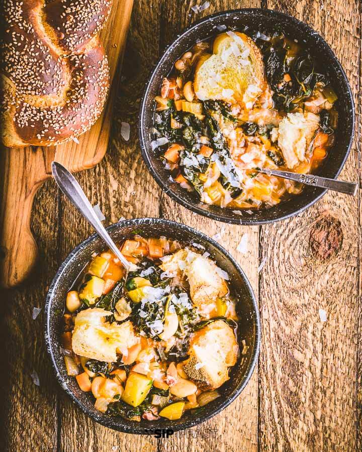 Two bowls of soup and loaf of bread on the table.