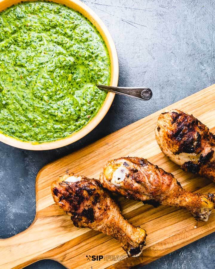 Chicken legs on cutting board and green sauce in a bowl.