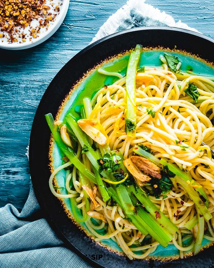 Overhead shot of plated spaghetti and celery on blue board.