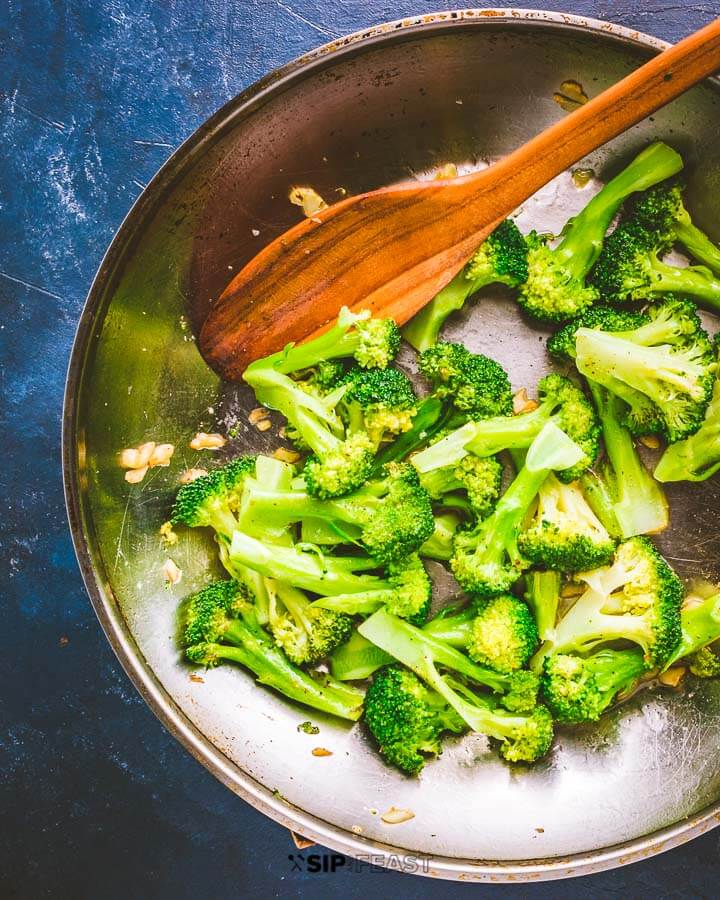 Sauteed garlic broccoli in pan on blue background.