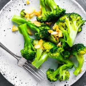 Cooked broccoli and garlic on white plate.
