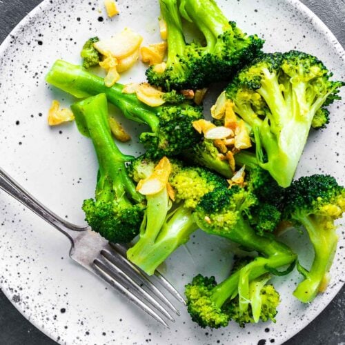 Cooked broccoli and garlic on white plate.