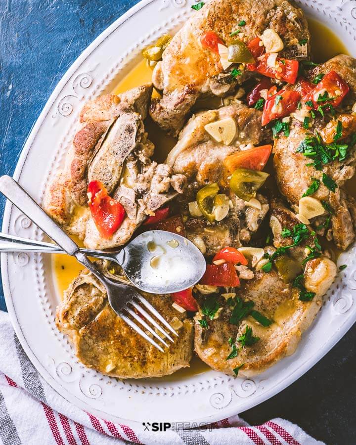 Platter of pork chops with cherry peppers on a blue background. 