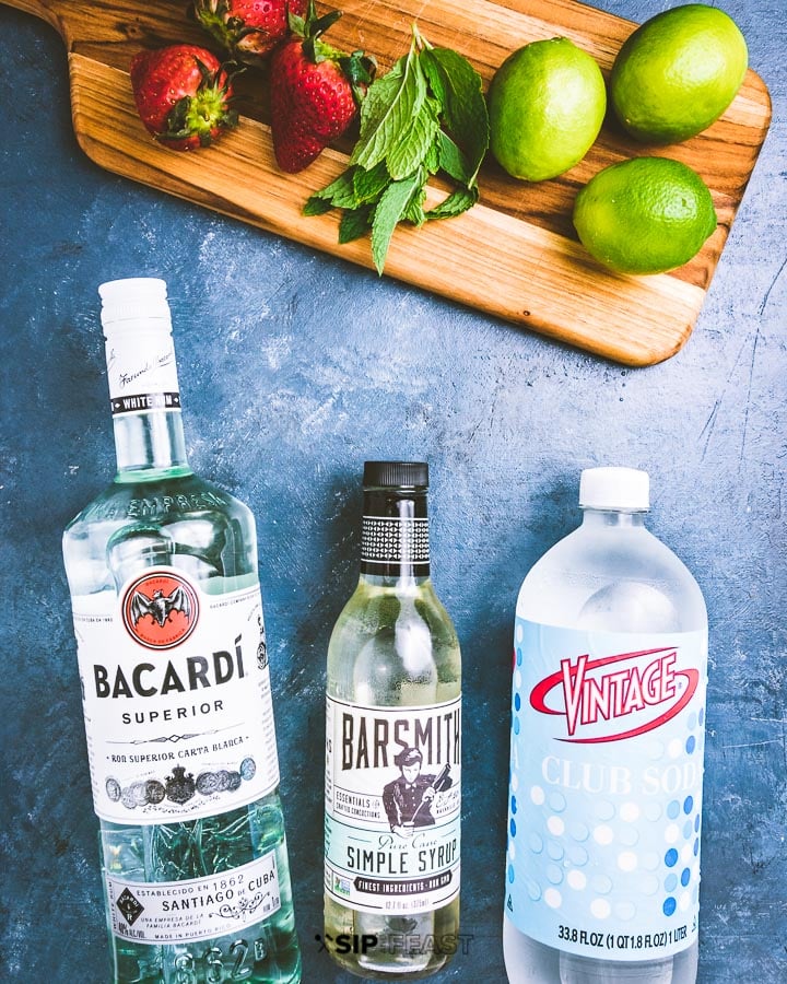 Cutting board with strawberries, mint and limes on a blue table alongside with Bacardi, straightforward syrup and membership soda. Strawberry Mojito Strawberry Mojito strawberry mojito