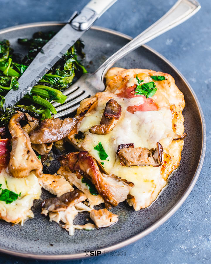 45 degree angle picture of chicken valdostana and broccoli rabe in grey plate on blue table.