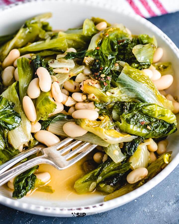 Escarole and beans in white bowl on blue table.