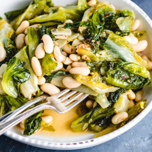 Escarole and cannellini beans in white bowl on blue table.