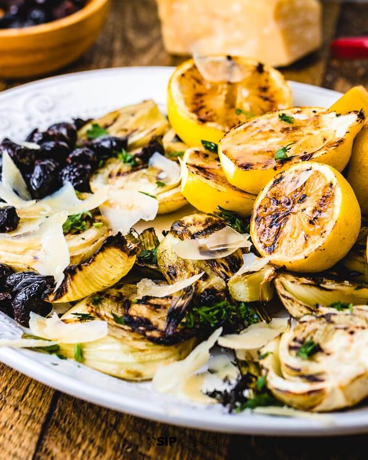 Fennel salad in plate with a block of parmesan, a vegetable peeler and a bowl of olives in background.