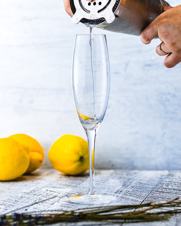 Pouring drink in champagne flute with 3 lemons in background. 