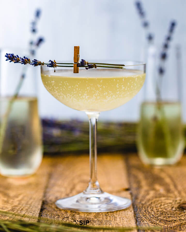 Cocktail with champagne flutes in background and fresh lavender on wood table.