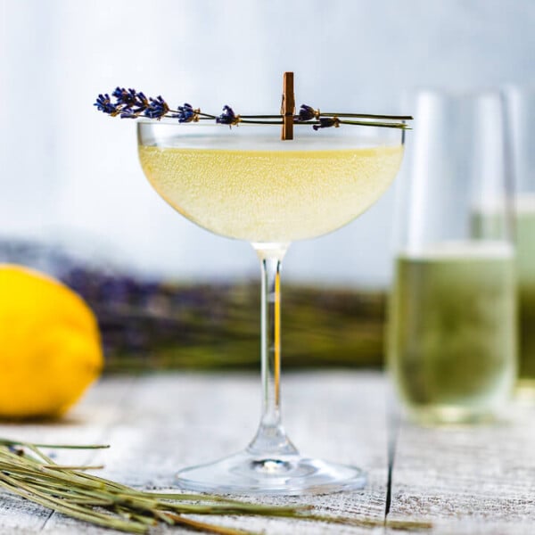 Glass of Lavender French 75 with champagne flutes, lemons and lavender in the background.
