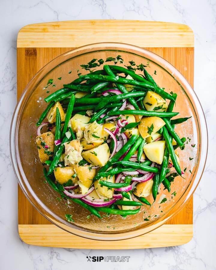 Potato green bean salad in glass bowl on cutting board.