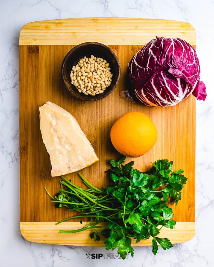 Ingredients shown on cutting board: pine nuts, radicchio, parmigiano reggiano, 1 orange and fresh parsley.