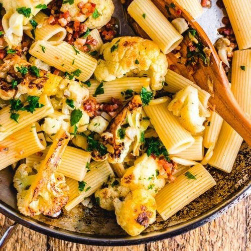 Rigatoni, cauliflower and bacon in pan on wooden table.