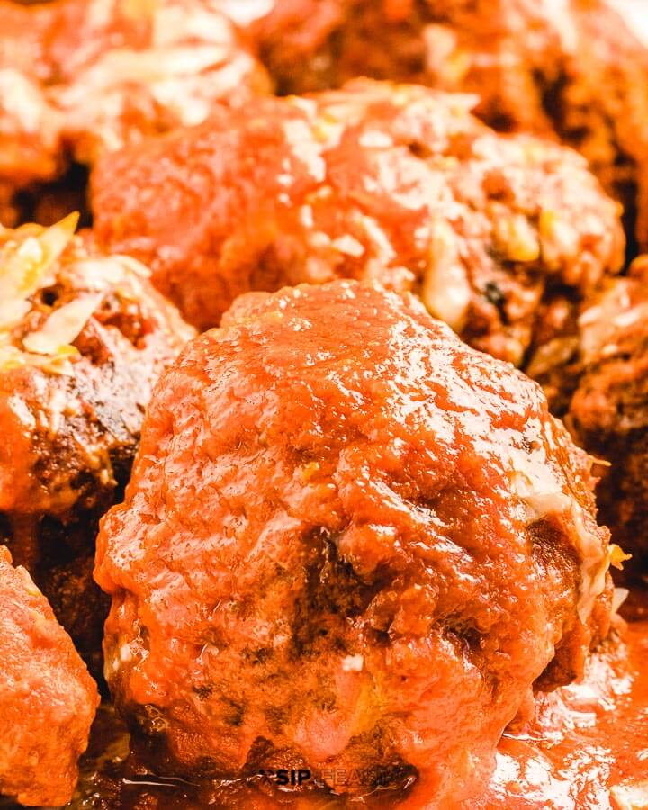 Close up picture of 1 large meatball with sauce.