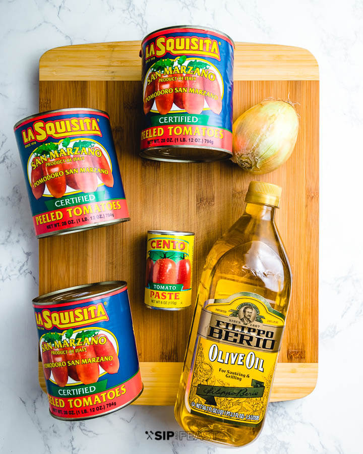 Ingredients shown: 3 cans San marzano plum tomatoes, can of tomato paste, onion, and olive oil on cutting board.