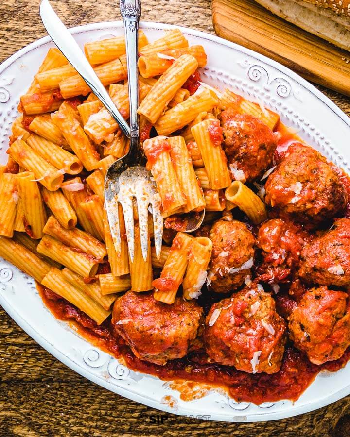 White platter of pasta with sauce and meatballs.