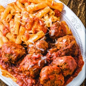 Meatballs and pasta in platter on wood table.