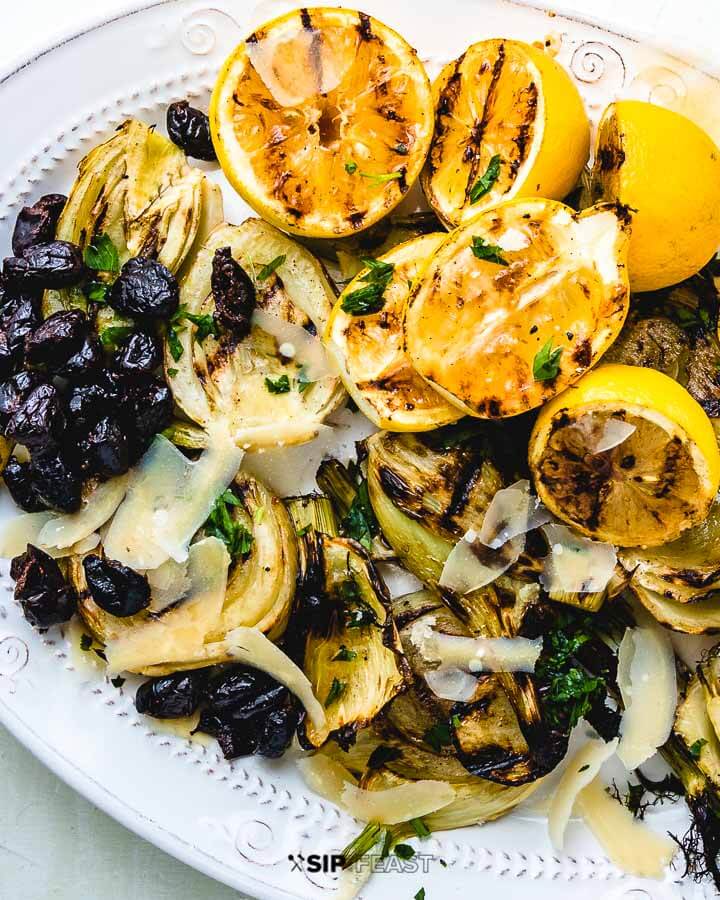 Fennel, lemons and black olives on white plate on green background.