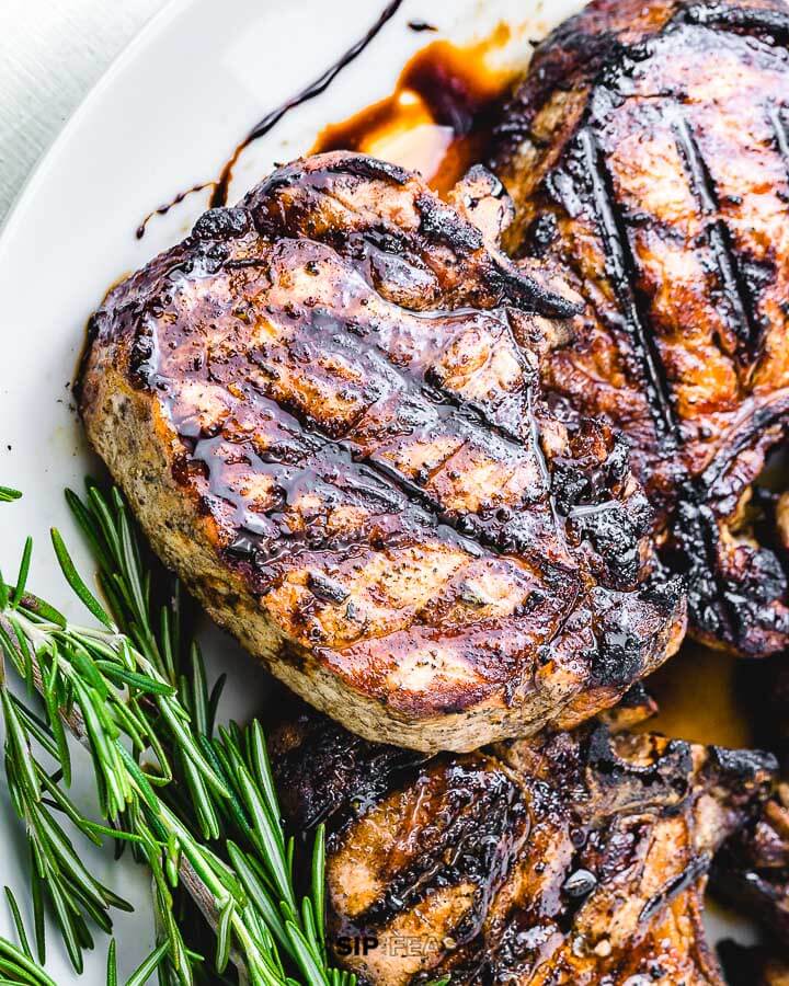 Grilled pork chop in white plate with rosemary garnish.