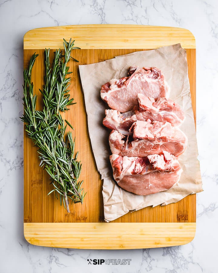Four pork chops and bunch of rosemary on cutting board.