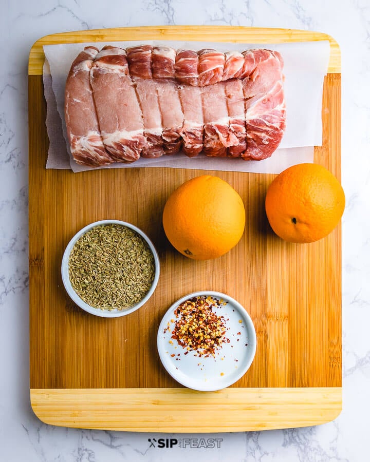 Ingredients shown: pork loin, oranges, bowl of fennel seeds and chili flakes on cutting board.