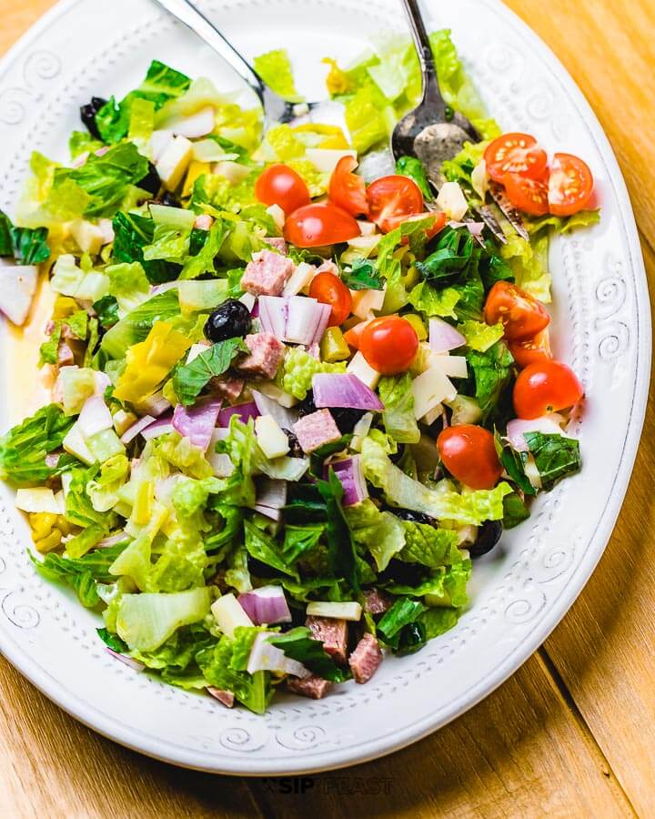 Italian chopped salad in white plate on wood table.