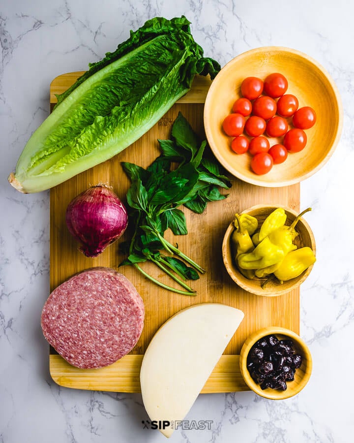 Ingredients shown: romaine lettuce, cherry tomatoes, basil, red onion, salami, provolone, Tuscan peppers and oil cured olives.