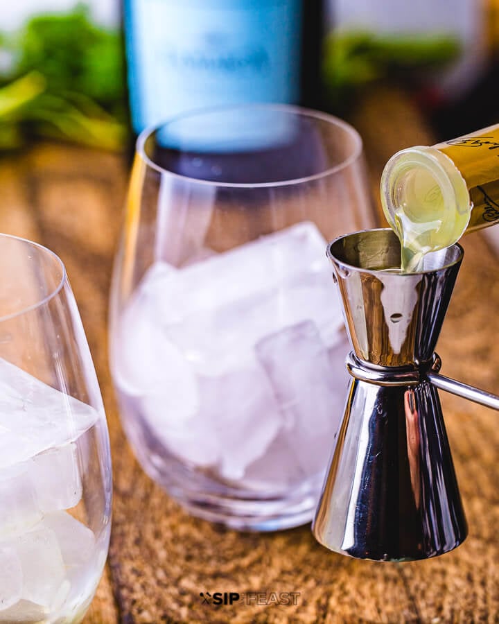 Limoncello being poured into a cocktail jigger and a wine glass filled with ice.