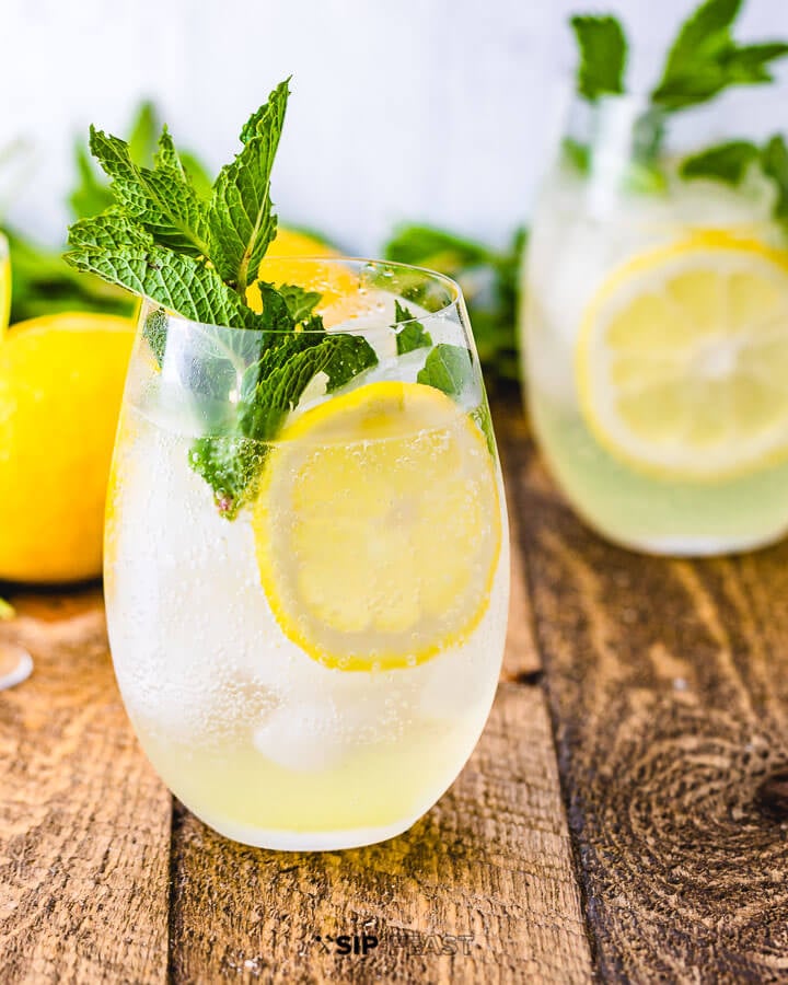 Two glasses of the Limoncello spritz with mint, lemon slices and two lemons in the background.