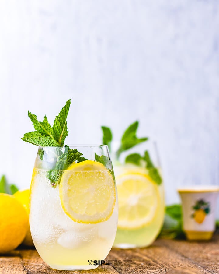 Two glasses of limoncello spritz with mint and lemon and a glass of limoncello in the background.